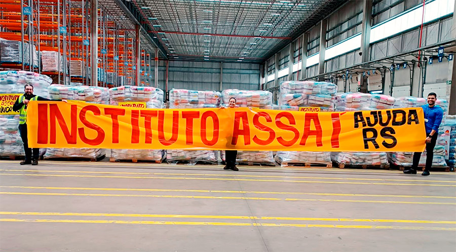 Colaboradores do Assaí no Centro de Distribuição Assaí Cajamar em São Paulo estão à frente dos cobertores que serão doados pelo Instituto Assaí para as vítimas das enchentes no Rio Grande do Sul. Eles seguram uma faixa com a frase 'Instituto Assaí Ajuda Rio Grande do Sul'